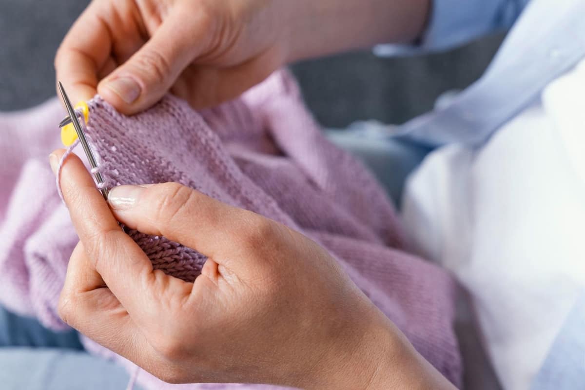 Coussin tricoté géométrique, pelotes de laine et aiguilles sur une table en bois