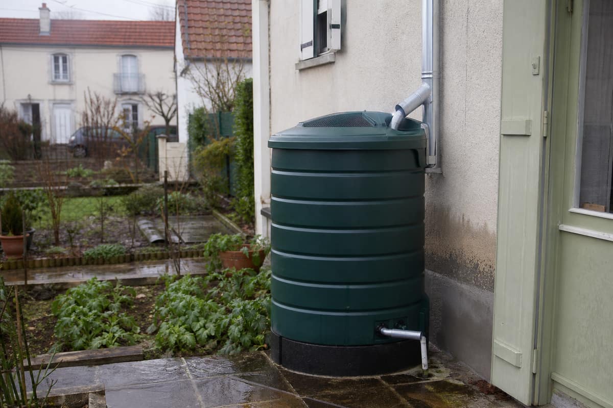 Cuve de récupération d’eau de pluie reliée à une gouttière dans un jardin