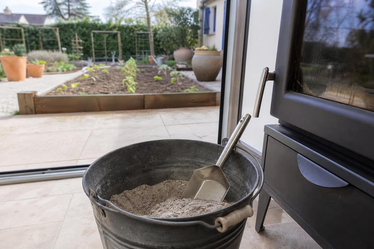 Seau métallique de cendres de pellets près d’un potager au printemps