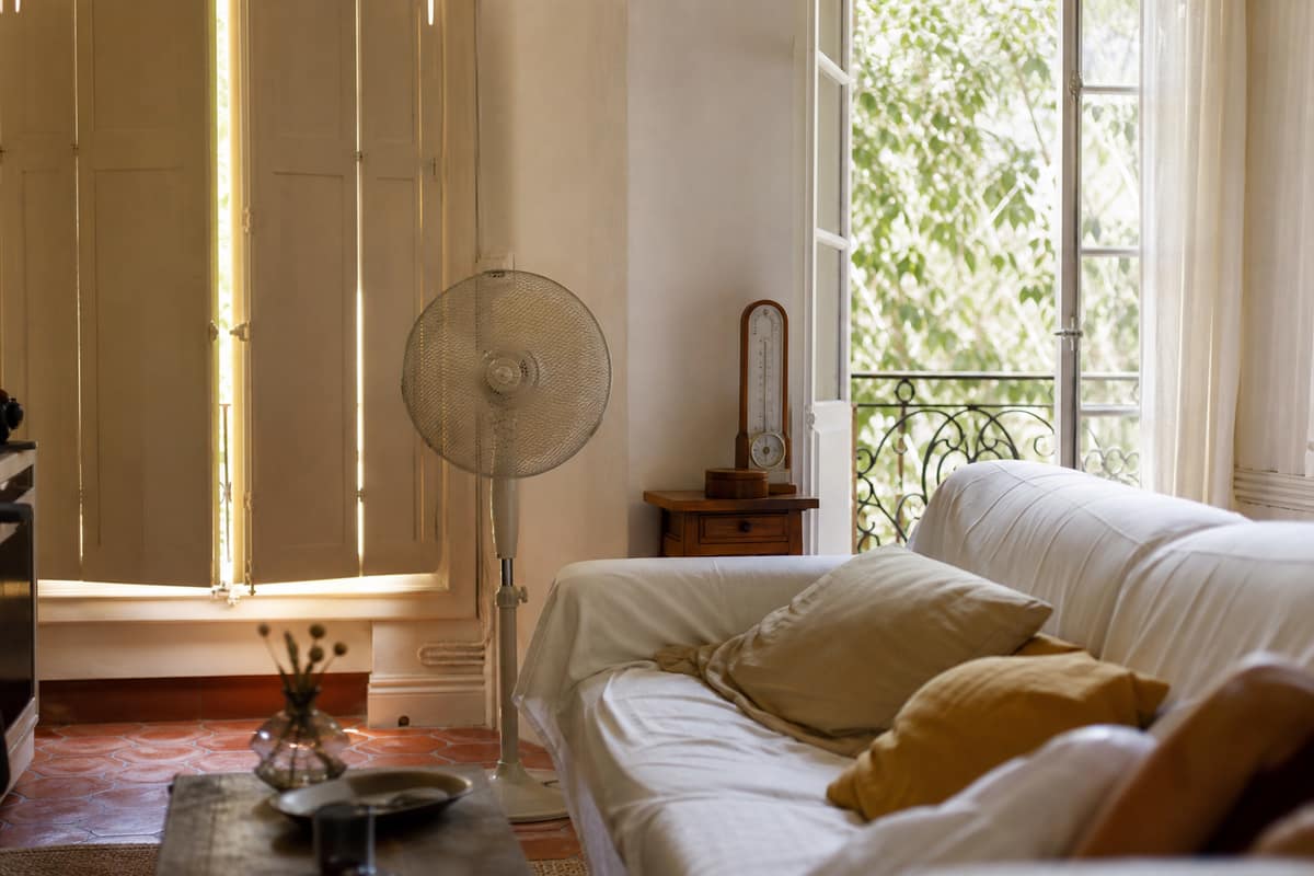Salon français ombragé avec volets fermés, ventilateur et lumière estivale filtrée