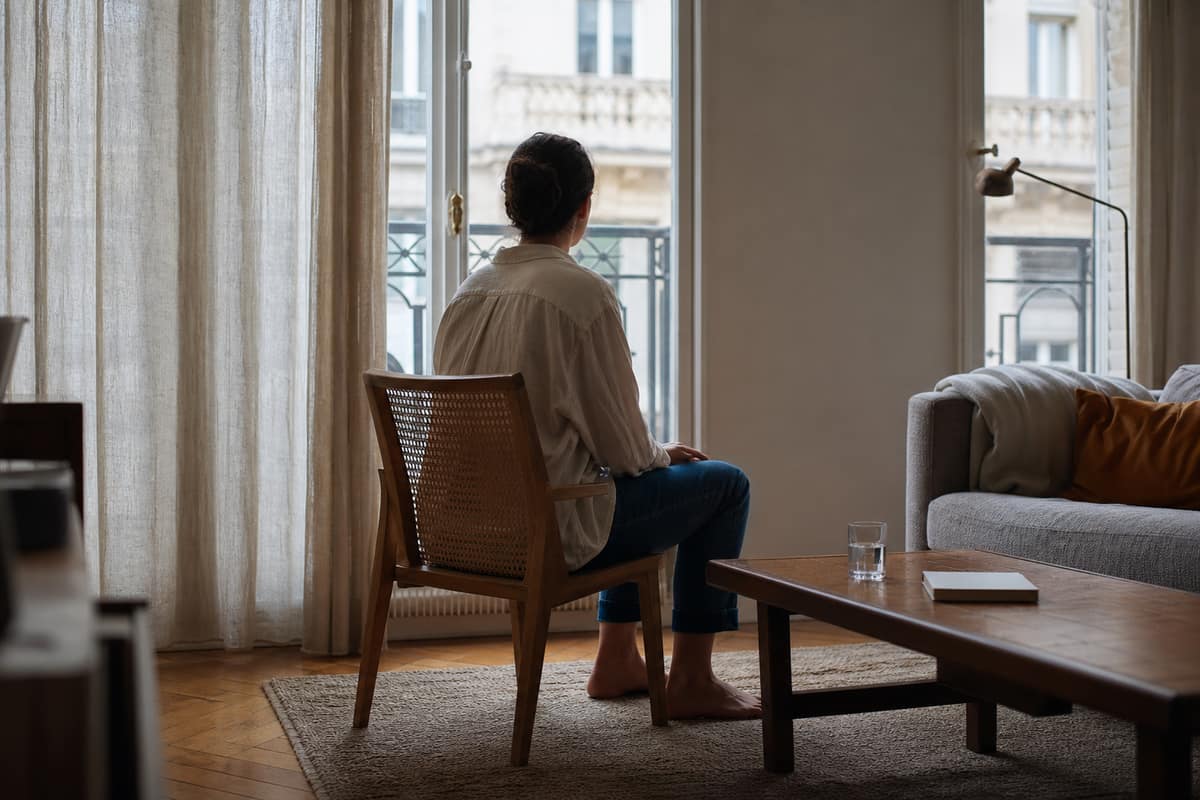 Personne assise près d’une fenêtre, carnet et verre d’eau sur une table
