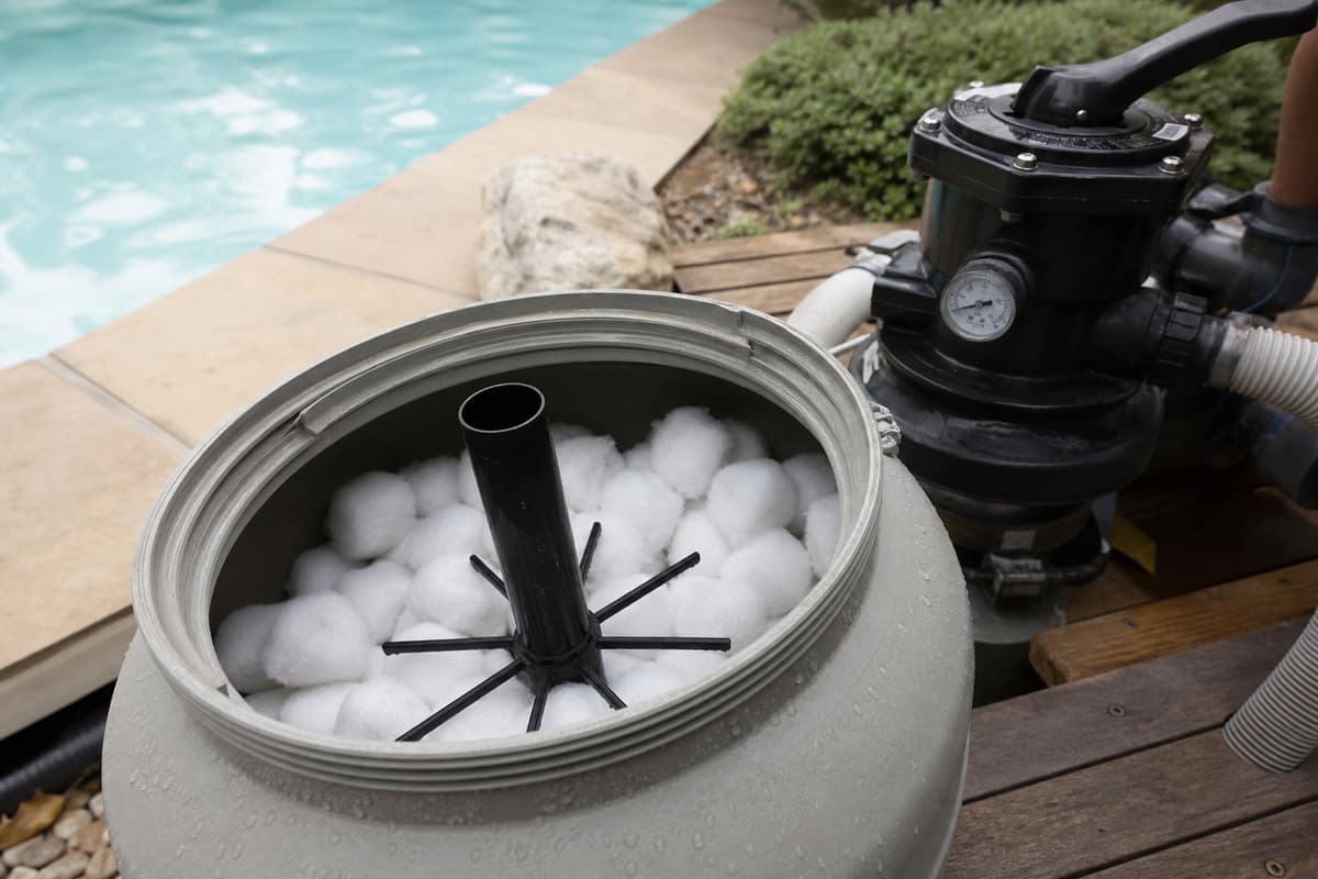 Boules filtrantes blanches près d’un filtre à sable de piscine ouvert