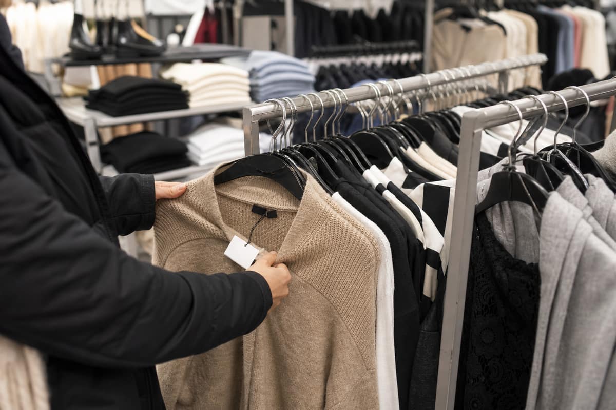 Portants de vêtements en déstockage dans une boutique française, mains vérifiant un tissu