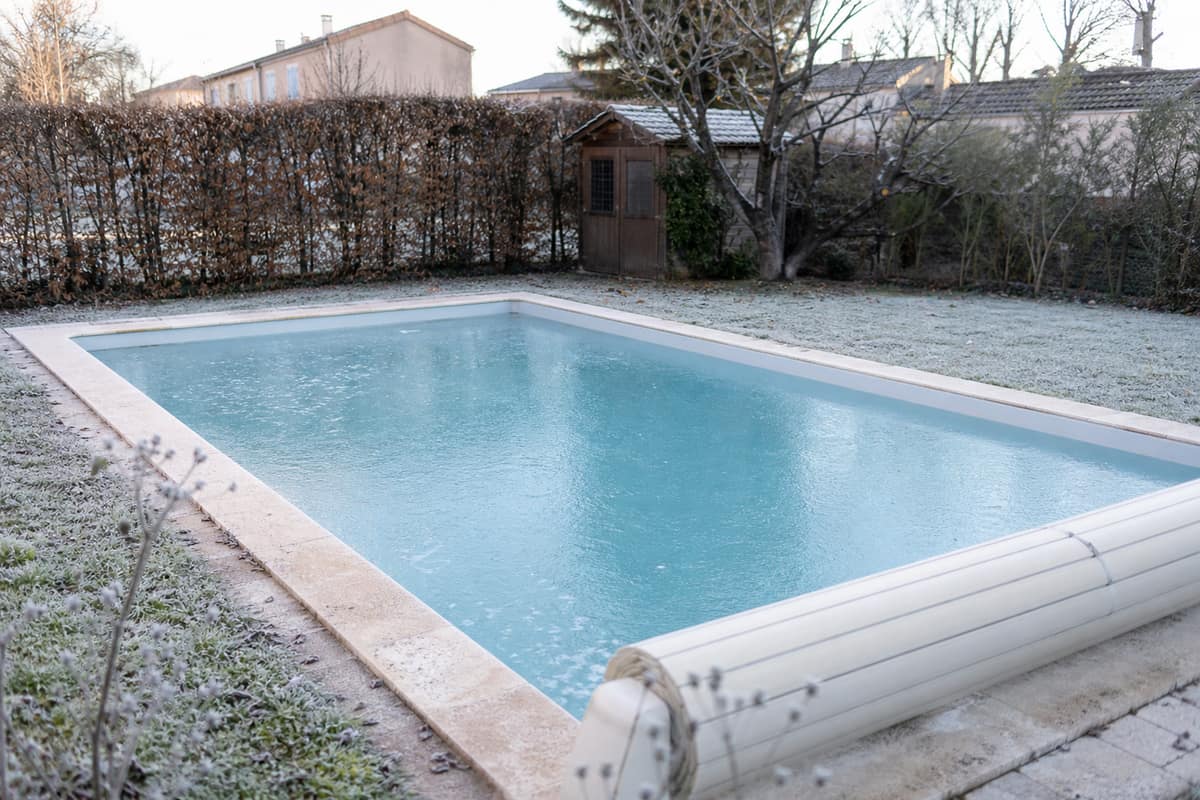 Piscine enterrée couverte d’une fine couche de glace dans un jardin d’hiver