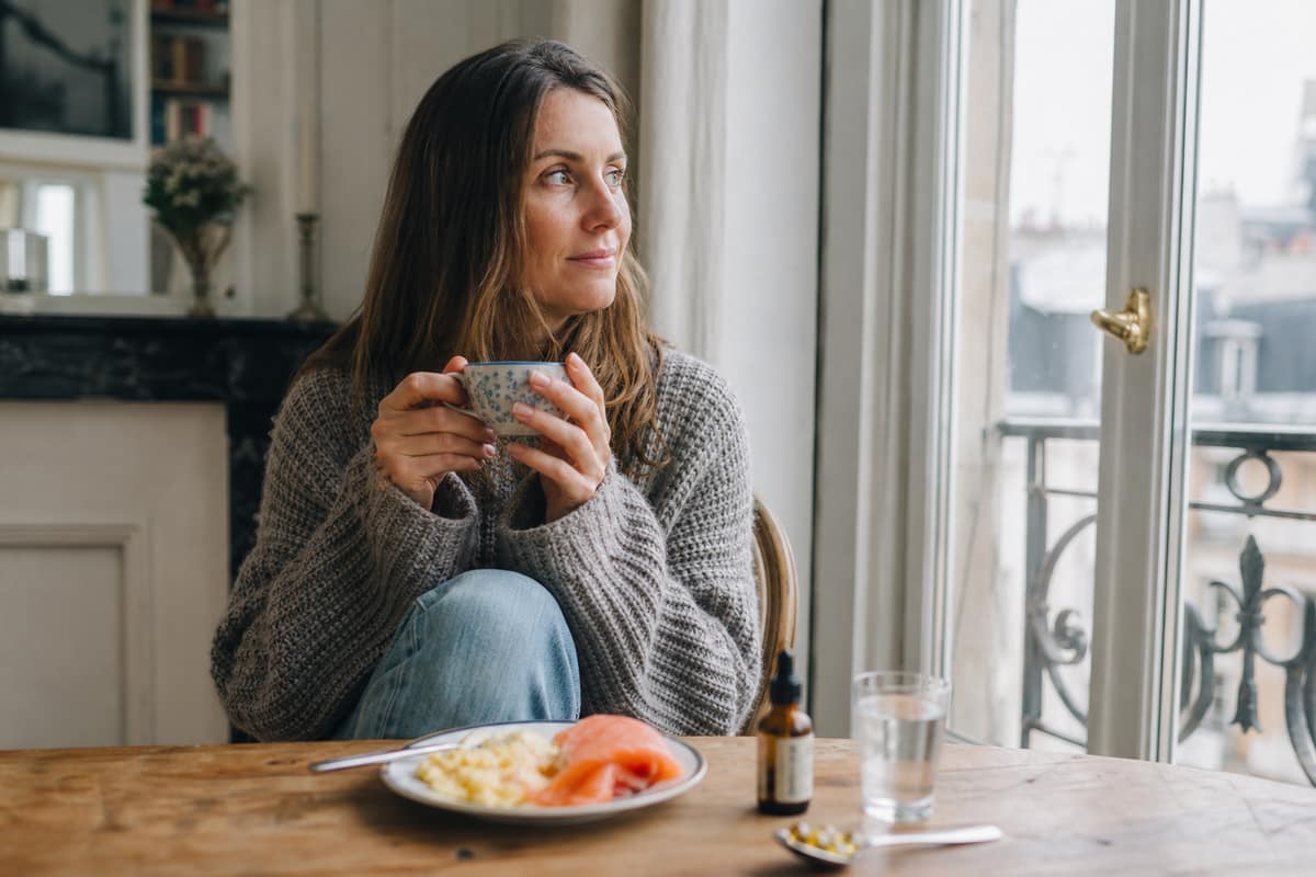 Femme prenant son petit-déjeuner près d’une fenêtre lumineuse un matin d’hiver
