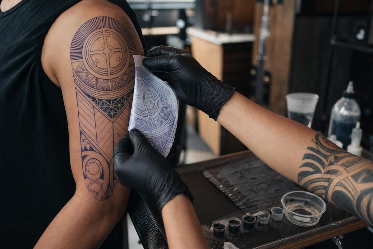 Tatoueur préparant un motif géométrique noir sur le bras d’un client