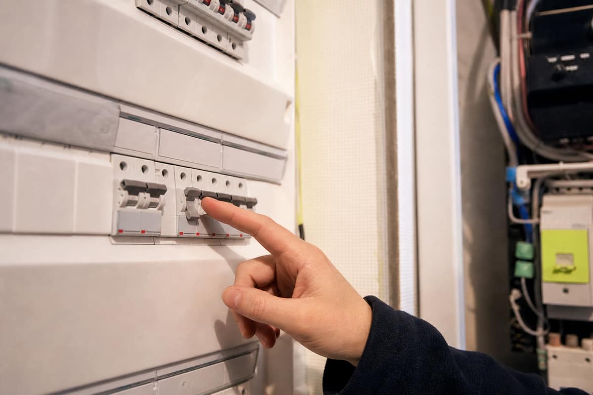 Main approchant un disjoncteur du tableau électrique dont l'un des interrupteurs est coupé