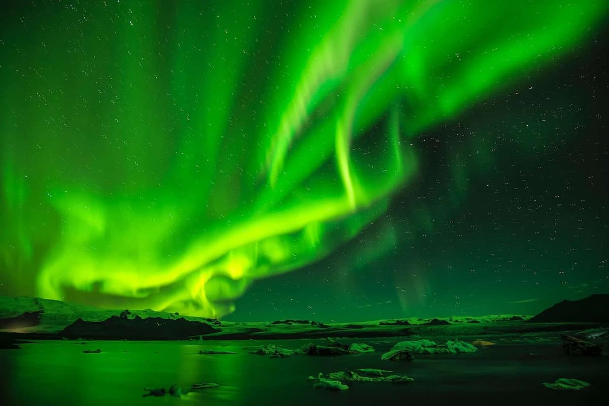 Aurore verte au-dessus d’un lac gelé et de chalets en Laponie.