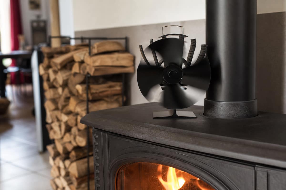 Ventilateur thermoélectrique noir posé sur un poêle à bois en fonte