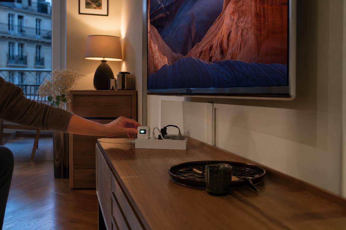 Téléviseur mural et wattmètre branché sur une multiprise dans un salon
