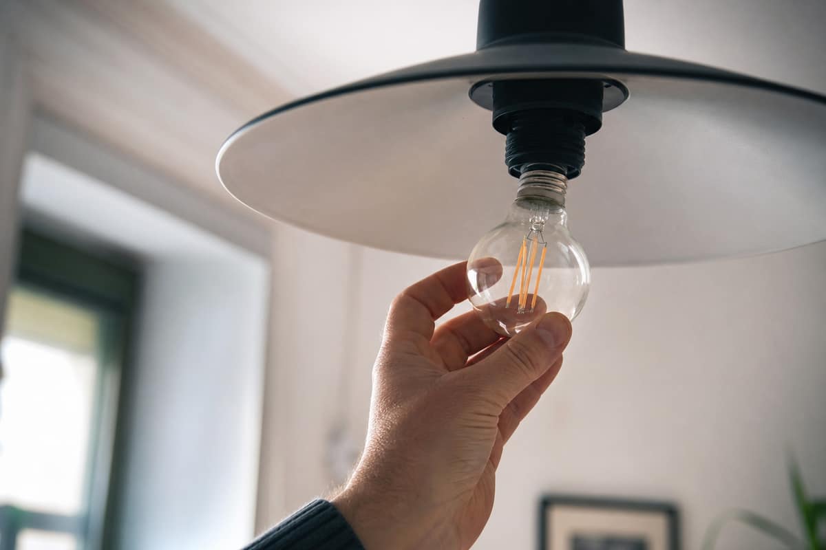 Main qui remplace une ampoule dans un luminaire de plafond