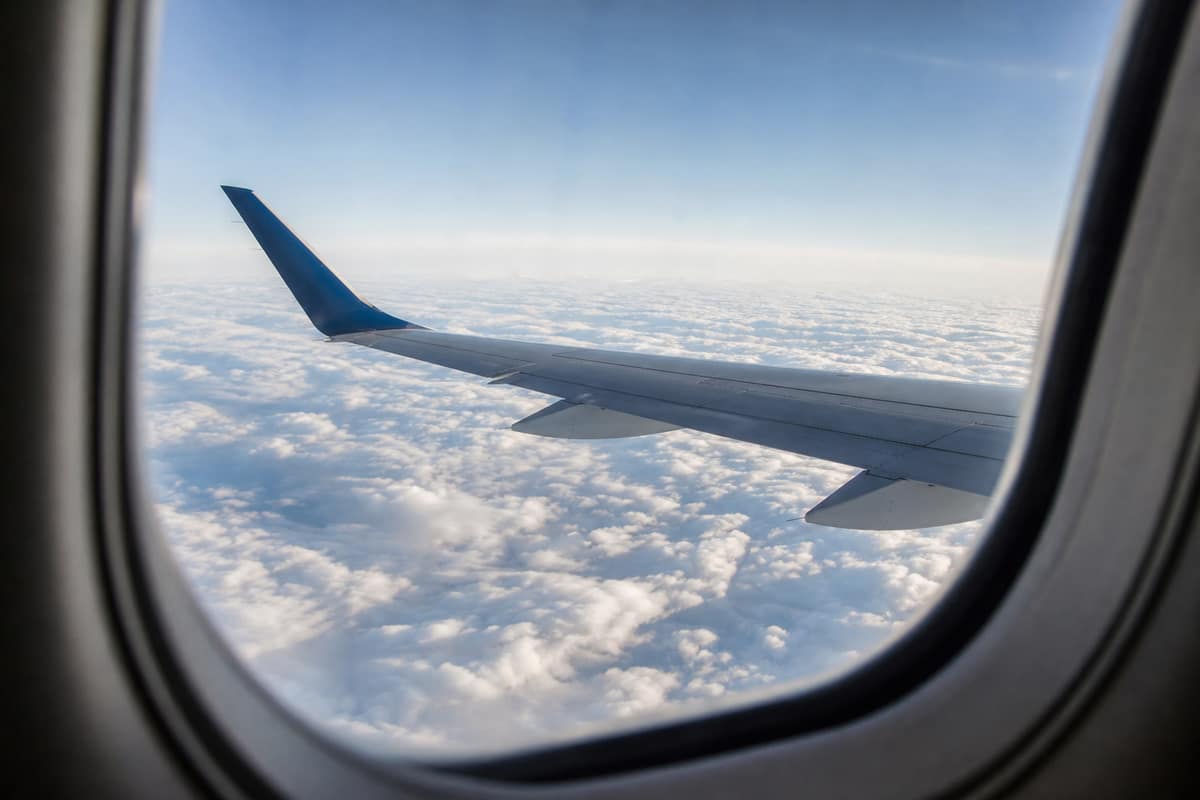 Aile d'avion vue par le hublot au-dessus des nuages en altitude