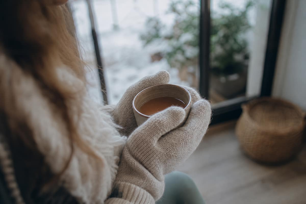 Personne réchauffant ses mains gantées autour d'une tasse chaude